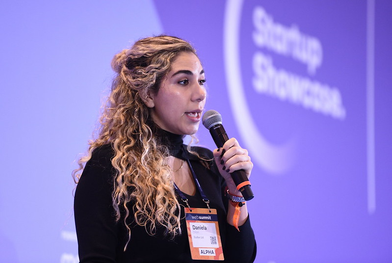 Person stands in front of wall with text that reads Startup Showcase. They are holding a microphone and appear to be speaking.