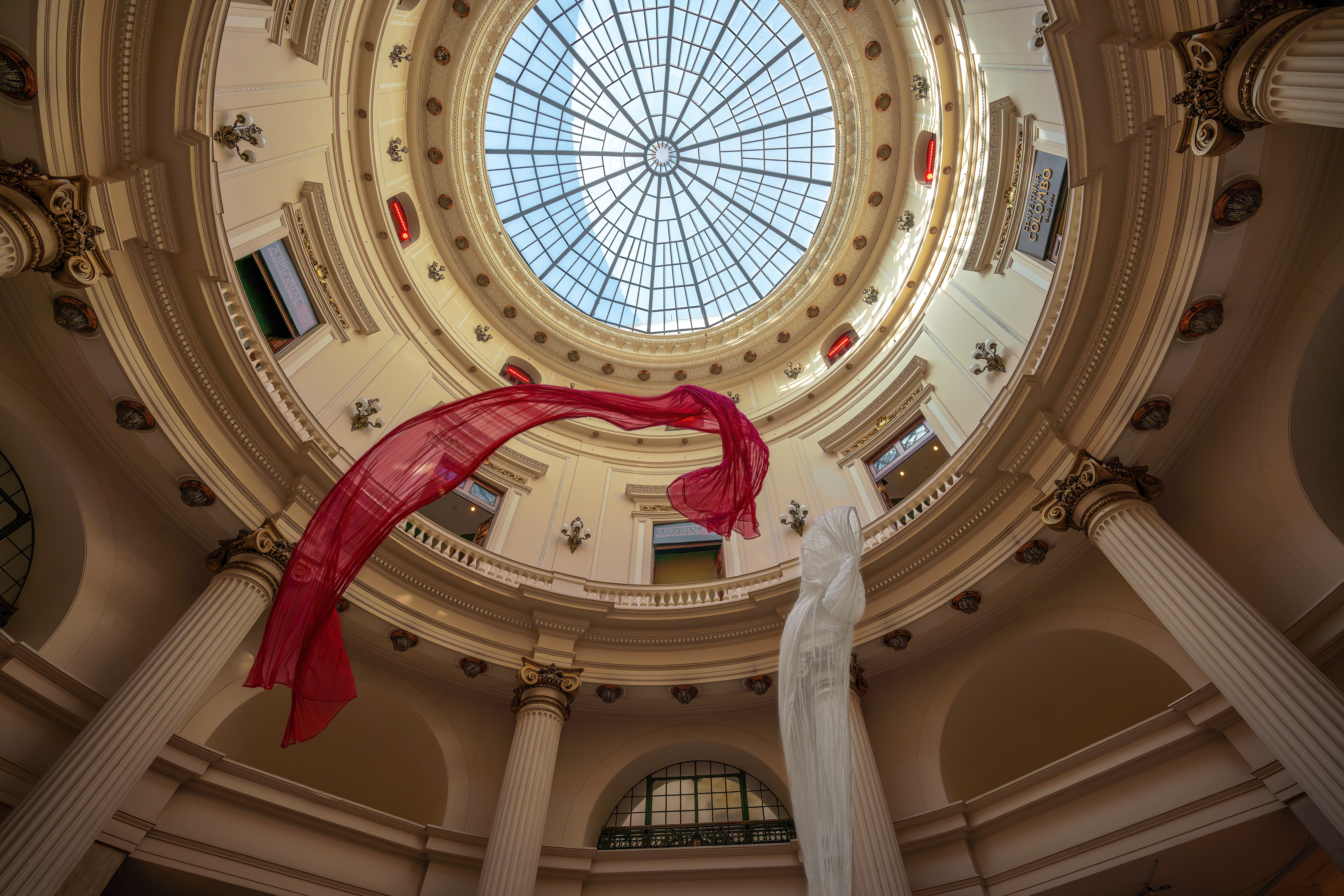 The interior of a circular room, under a dome. Roman-style columns or pillars are spaced around what's visible of the curved wall. At the top of the dome, a circular glass window offers a glimpse of the sky. Two diaphanous pieces of cloth appear to be floating down from the ceiling. Image: Diego Grandi/Shutterstock.