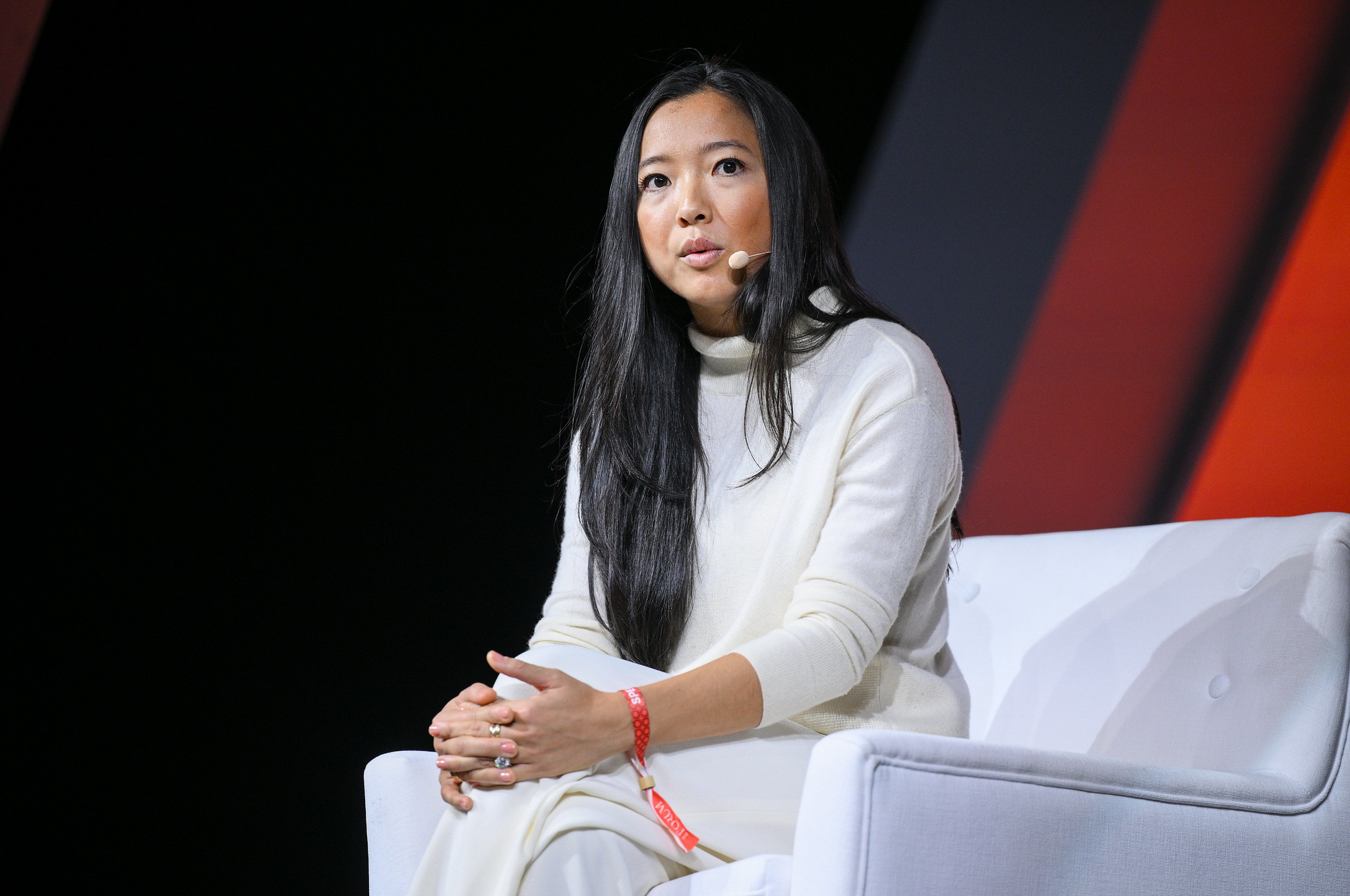 A person (Siam Capital founder and general partner Sita Chantramonklasri) sits in an armchair. Their left leg is crossed over their right. They're clasping their left knee with both hands, and their fingers are interlocked. They are wearing a headset mic, and appear to be speaking. This is onstage at Web Summit.