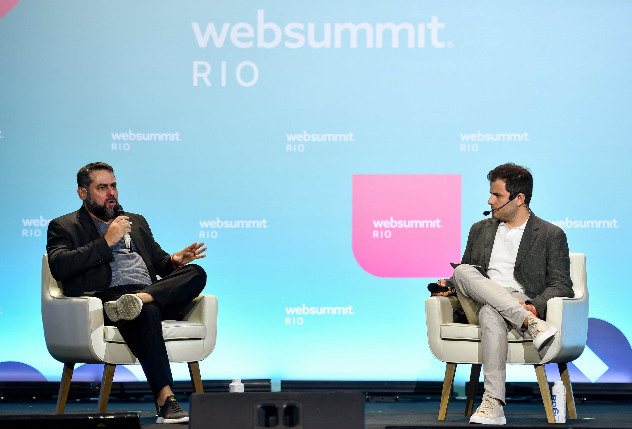 Two male presenting speakers (left to right)  Eve Air Mobility CEO André Stein and Diogo Teixeira, co-owner and publisher of Razão Automóvel, speaking on stage at Web Summit Rio 2023.