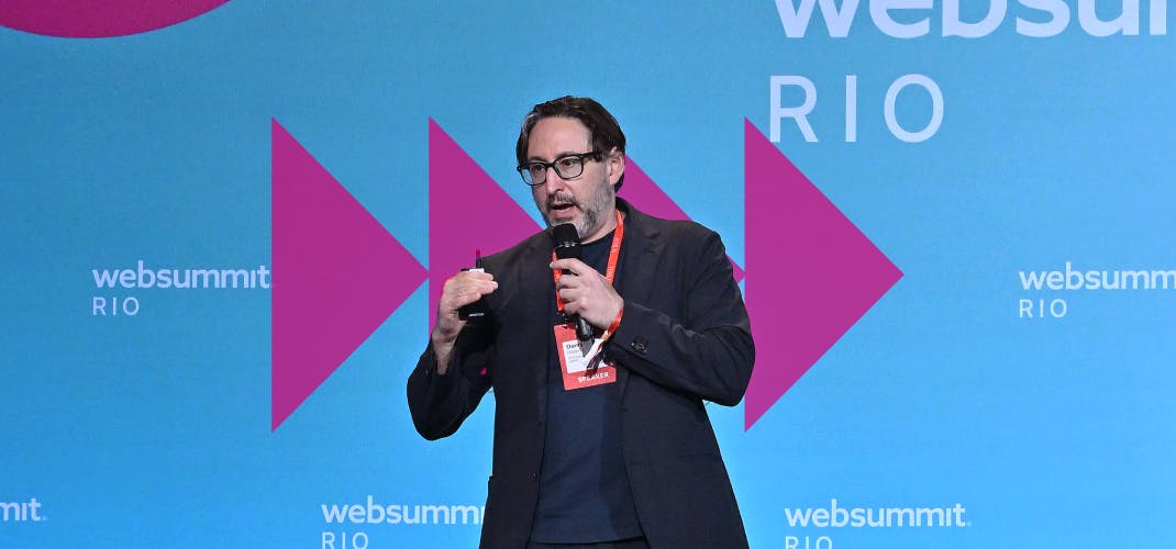 An image of Dorry Segev, professor of epidemiology and Surgery at NYU Langone Health. Dorry is holding a microphone in one hand, and what appears to be a presentation clicker in the other. Dorry appears to be speaking. The Web Summit Rio logo appears in several places on the wall behind Dorry.