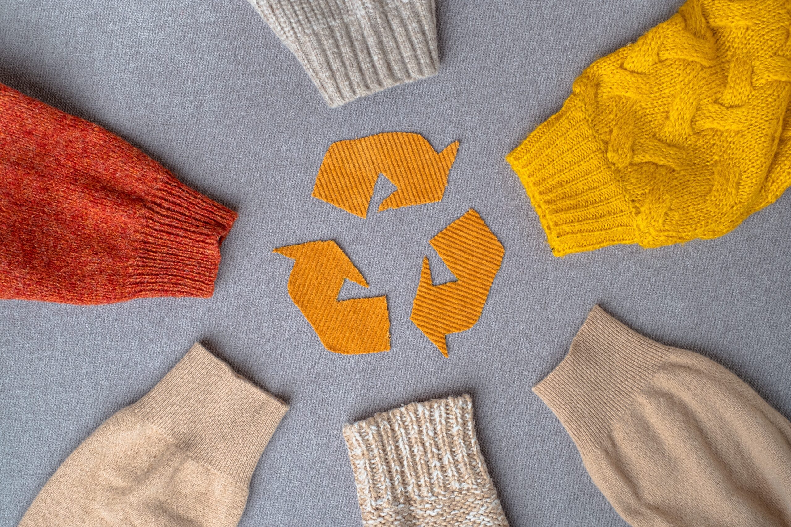 Six jumper sleeves are circled around a recycling symbol, showing sustainable fashion clothing is an option