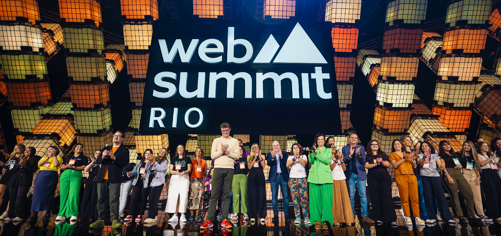 A group of people including Web Summit founder and CEO Paddy Cosgrave stand on a stage. A large Web Summit Rio sign is suspended above them. These are some of the women founders attending Web Summit Rio 2024.