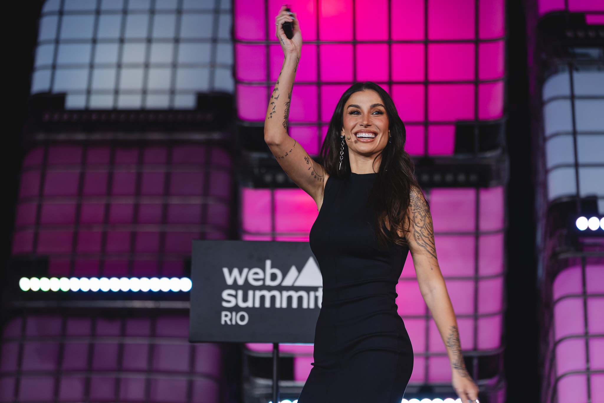 Image of a person, Bianca Andrade, CEO and founder of Boca Rosa, on Center Stage at Web Summit Rio 2024. Bianca is walking out on stage, smiling and holding a microphone in the right hand.