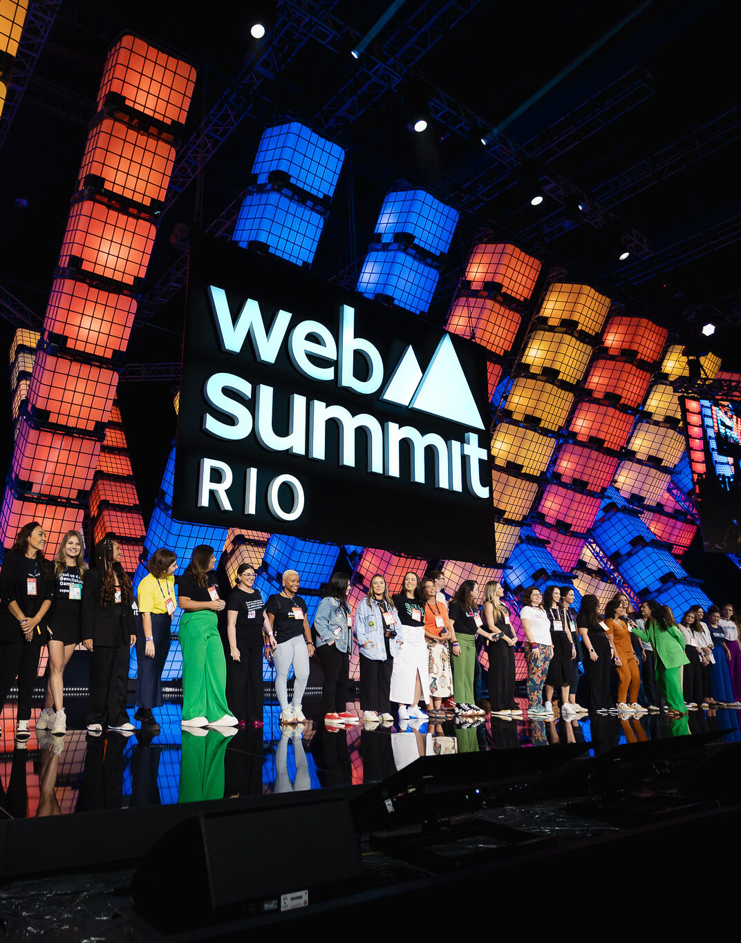 Photograph of women founders on Center Stage at Web Summit Rio. There is a row of women standing on stage with the Web Summit Rio logo lit up behind them.